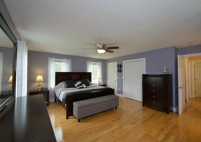 bedroom with baseboards, light wood-style flooring, ceiling fan, and two closets