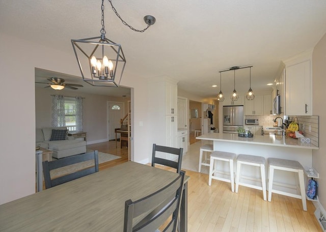 dining space with light wood-style floors, stairs, and ceiling fan with notable chandelier