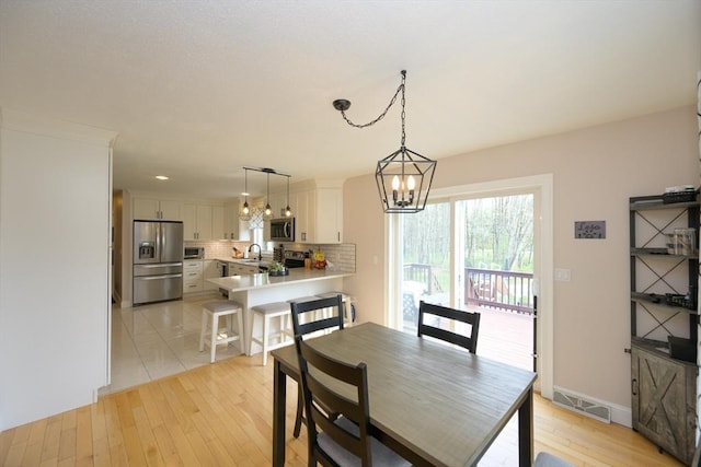 dining area featuring baseboards, a notable chandelier, light wood finished floors, and visible vents