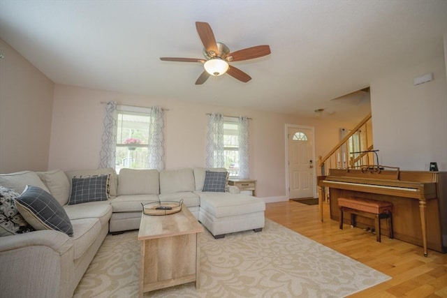 living room featuring light wood-style floors, a ceiling fan, and stairs