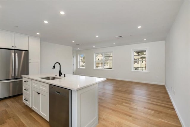 106 Broadway, Salem, MA 01970 - kitchen with stainless steel appliances, a sink, white cabinetry, light wood-style floors, and an island with sink