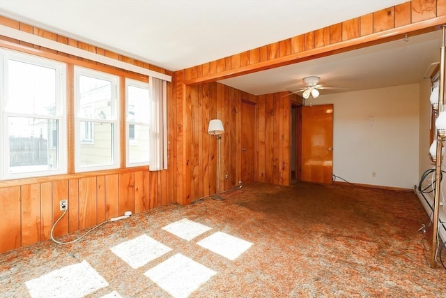 carpeted empty room featuring wood walls and a ceiling fan