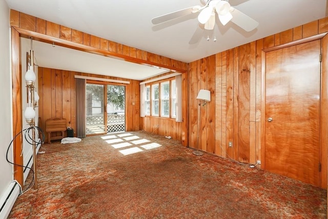 spare room featuring carpet floors, wood walls, a ceiling fan, and a baseboard radiator