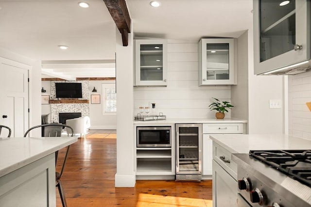 kitchen featuring a large fireplace, beverage cooler, stainless steel microwave, light countertops, and beam ceiling