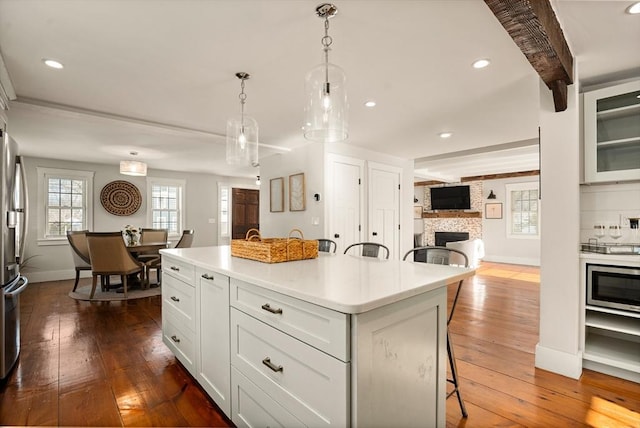 kitchen with dark wood-type flooring, light countertops, beamed ceiling, and a kitchen bar