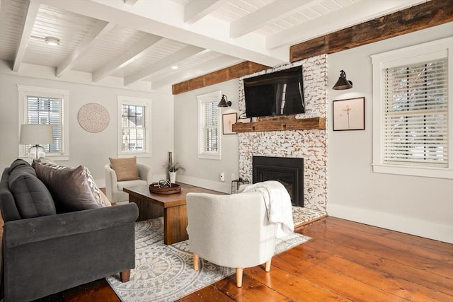 living area with a large fireplace, beam ceiling, baseboards, and hardwood / wood-style flooring