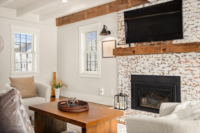 living area with a glass covered fireplace, beamed ceiling, baseboards, and wood finished floors