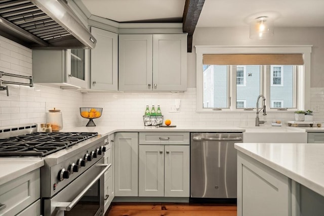 kitchen with light countertops, appliances with stainless steel finishes, ventilation hood, and a sink