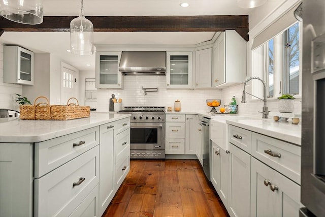 kitchen featuring dark wood-style floors, decorative light fixtures, stainless steel appliances, wall chimney range hood, and backsplash