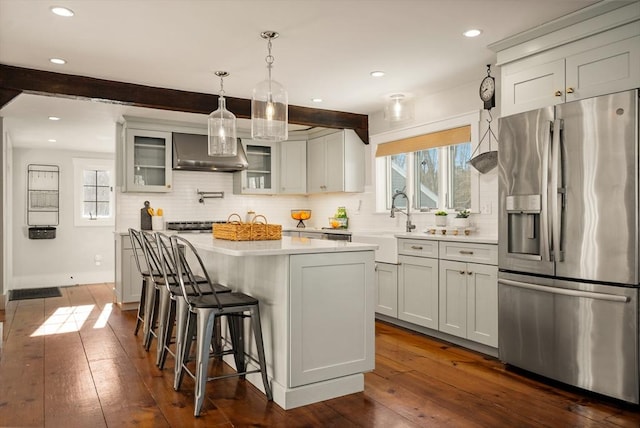 kitchen featuring dark wood-style floors, light countertops, wall chimney range hood, and stainless steel fridge with ice dispenser