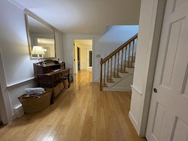 hallway with an inviting chandelier, stairway, light wood finished floors, and baseboards