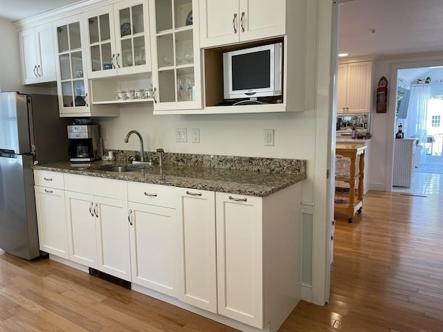 kitchen with dark stone countertops, light wood finished floors, freestanding refrigerator, and a sink
