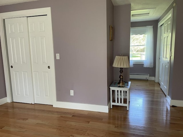 unfurnished bedroom with attic access, a baseboard radiator, wood finished floors, and baseboards