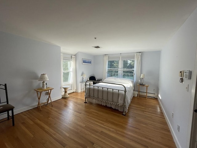 bedroom with baseboard heating, visible vents, wood finished floors, and multiple windows