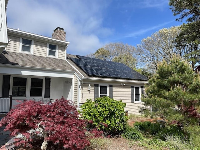 view of side of property featuring roof with shingles, a chimney, and solar panels