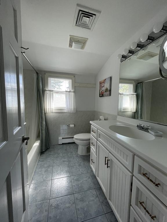 full bath with toilet, tile walls, baseboard heating, and a healthy amount of sunlight