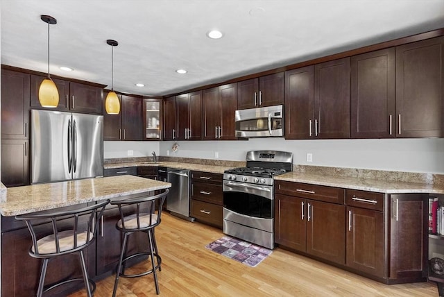 kitchen featuring dark brown cabinets, light stone countertops, light wood-style flooring, hanging light fixtures, and stainless steel appliances