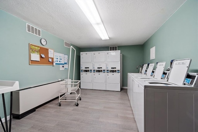 shared laundry area featuring light wood-style floors, stacked washer / dryer, washing machine and dryer, and visible vents