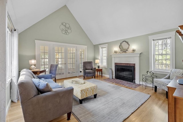 living room featuring a brick fireplace, high vaulted ceiling, french doors, and light wood-style floors