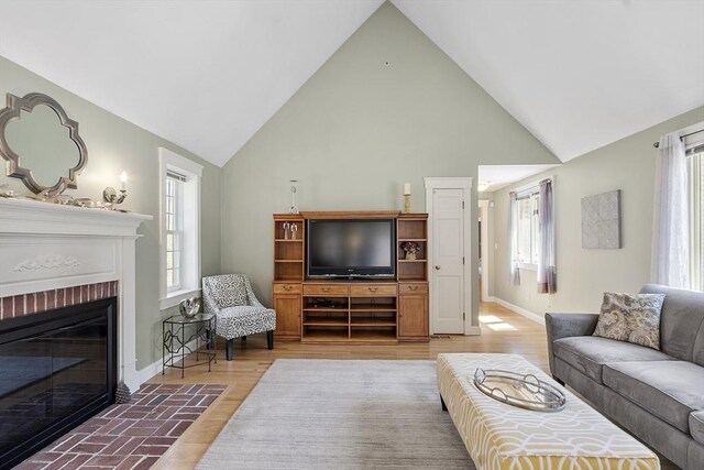living room featuring light wood-type flooring, baseboards, a fireplace, and high vaulted ceiling