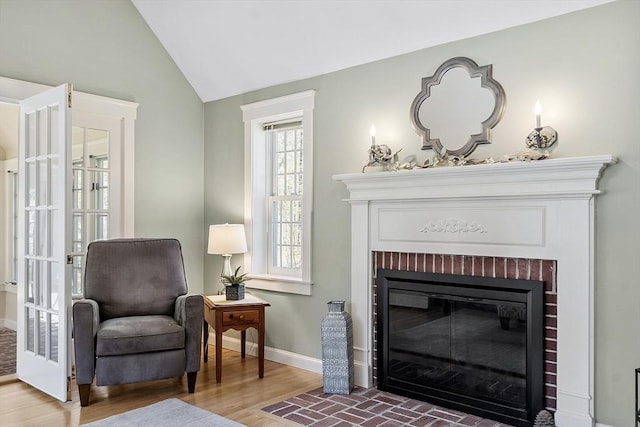 living area featuring baseboards, a fireplace, vaulted ceiling, and wood finished floors