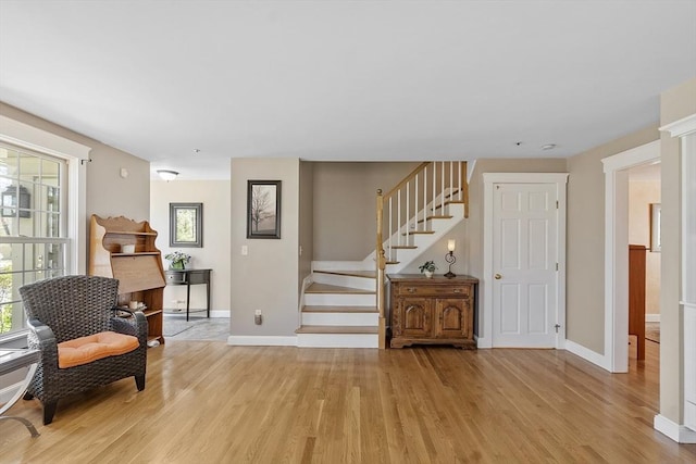 living area featuring baseboards, stairway, and light wood-type flooring