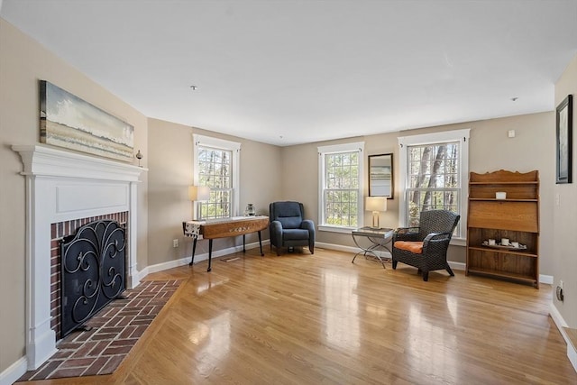 living area with baseboards, a brick fireplace, and wood finished floors