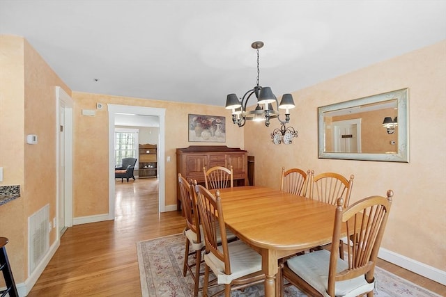 dining space with a chandelier, baseboards, visible vents, and light wood-type flooring