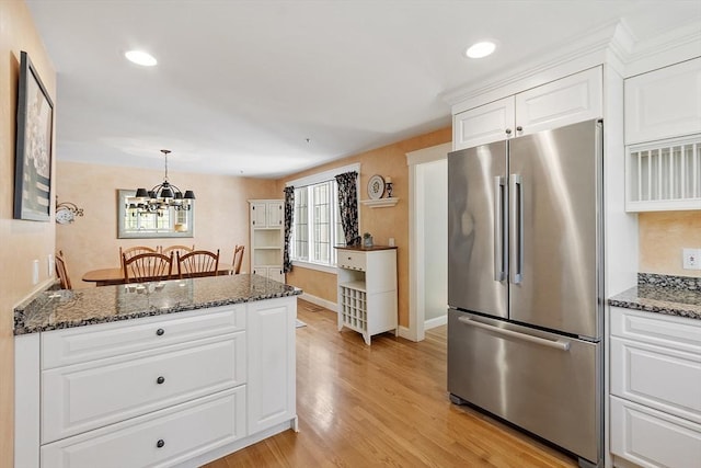 kitchen with freestanding refrigerator, light wood finished floors, an inviting chandelier, dark stone counters, and white cabinetry