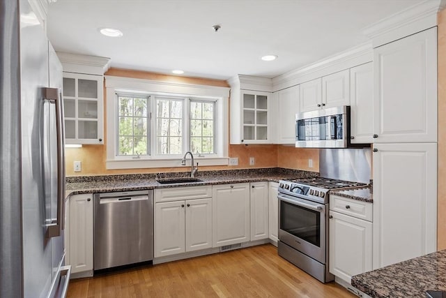 kitchen with glass insert cabinets, light wood-style floors, white cabinets, a sink, and appliances with stainless steel finishes
