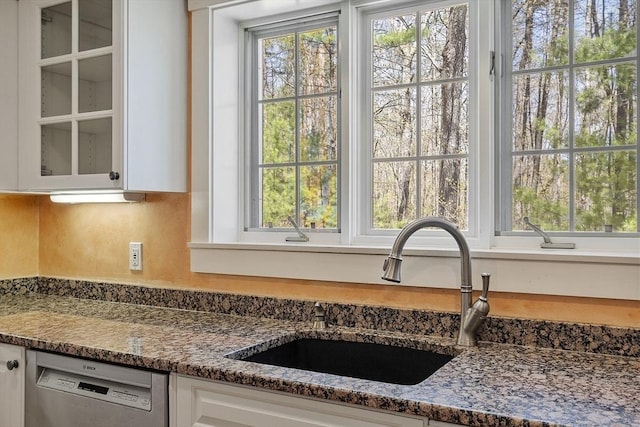 kitchen featuring plenty of natural light, dishwasher, a sink, glass insert cabinets, and white cabinetry