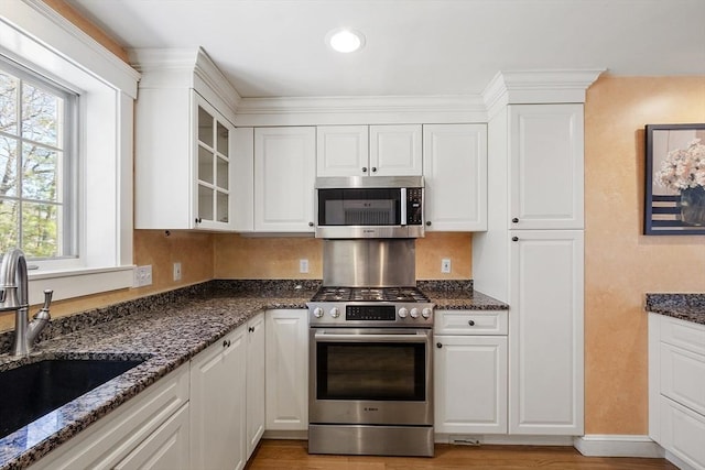 kitchen with appliances with stainless steel finishes, a sink, dark stone countertops, white cabinetry, and glass insert cabinets
