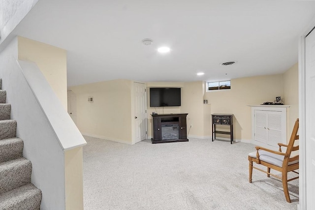 living area featuring light colored carpet, a glass covered fireplace, baseboards, visible vents, and stairway