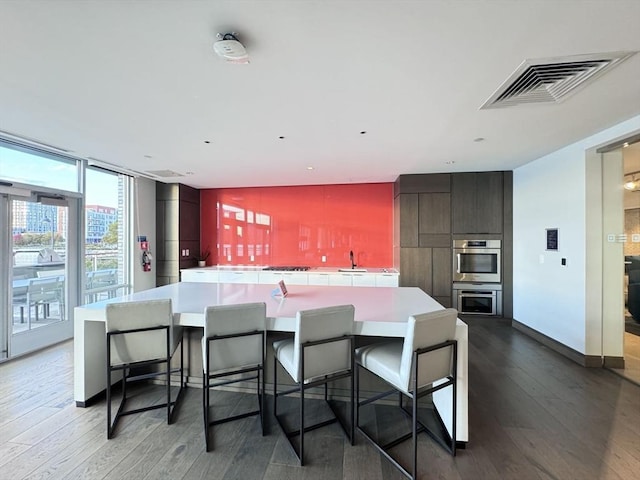 kitchen featuring a kitchen bar, stainless steel double oven, dark hardwood / wood-style floors, and a spacious island