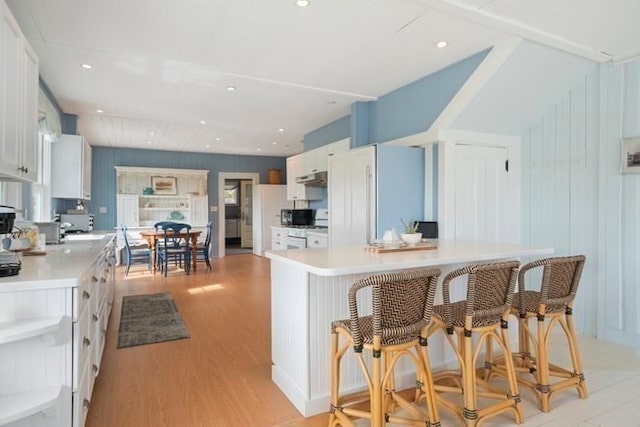 kitchen featuring a center island, range, white cabinets, light wood-type flooring, and a kitchen breakfast bar