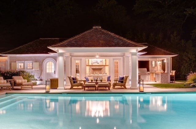 pool at twilight featuring a patio, an outdoor hangout area, and an outdoor kitchen