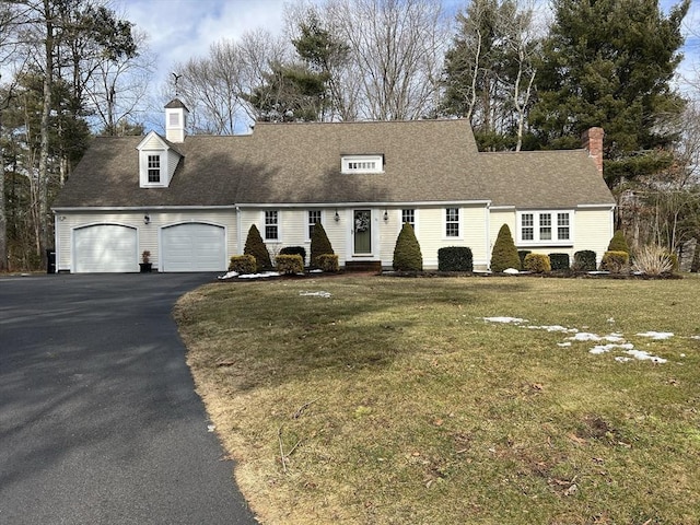 new england style home featuring an attached garage, a chimney, a front lawn, and aphalt driveway