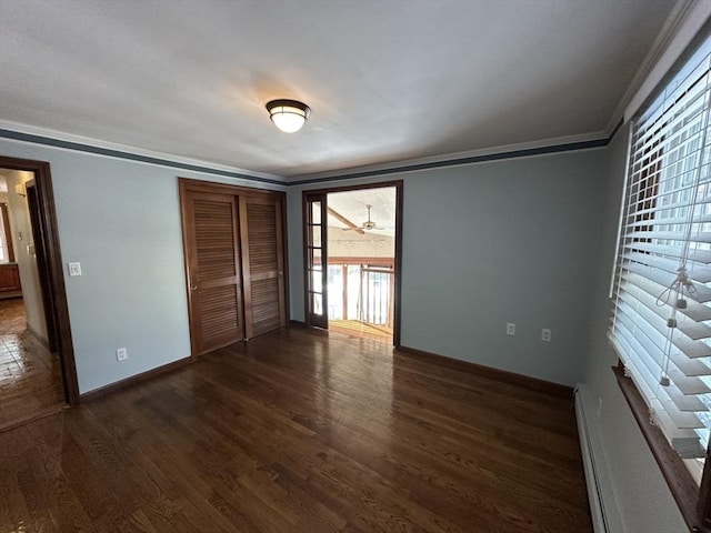 unfurnished bedroom featuring baseboard heating, crown molding, dark hardwood / wood-style flooring, and a closet