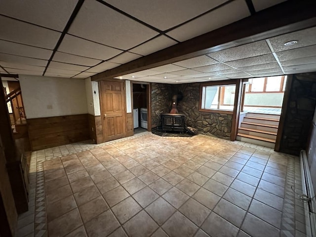 basement with a drop ceiling, tile patterned flooring, wood walls, and a wood stove