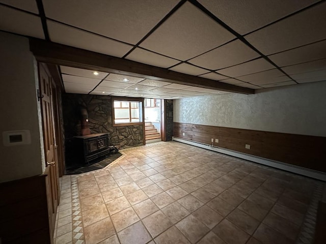 basement featuring a wood stove, light tile patterned floors, and a drop ceiling