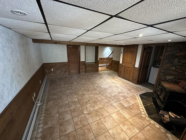 basement featuring light tile patterned floors, wooden walls, and a wood stove