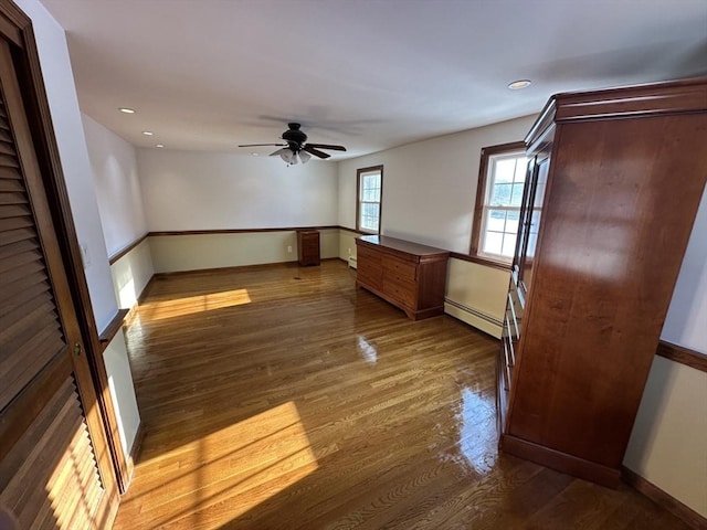 empty room featuring wood-type flooring, ceiling fan, and baseboard heating