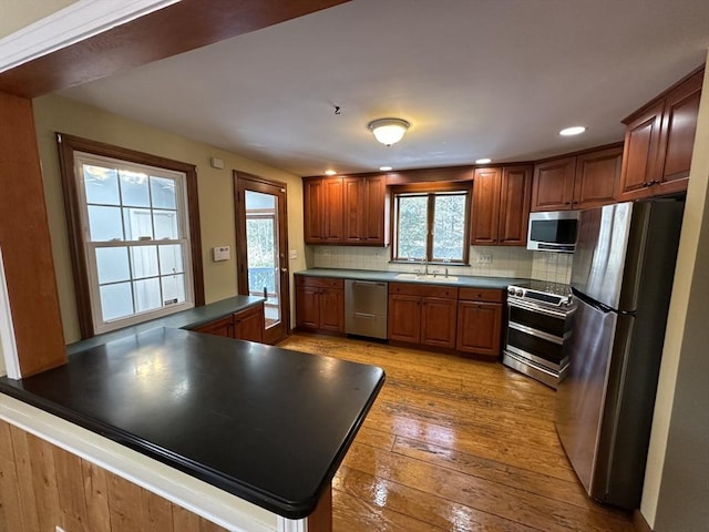 kitchen with appliances with stainless steel finishes, sink, decorative backsplash, kitchen peninsula, and light hardwood / wood-style flooring