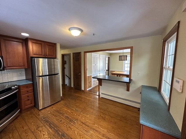 kitchen with a breakfast bar, appliances with stainless steel finishes, backsplash, dark hardwood / wood-style flooring, and a baseboard radiator