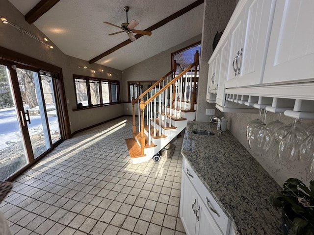 kitchen with white cabinetry, sink, vaulted ceiling with beams, light stone countertops, and a textured ceiling