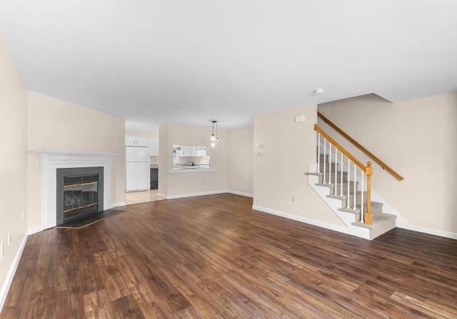 unfurnished living room with dark wood-style flooring, baseboards, stairway, and a fireplace with flush hearth