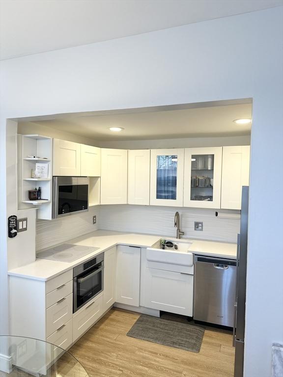 kitchen featuring sink, stainless steel appliances, light wood-type flooring, and white cabinetry