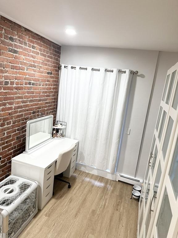 home office featuring brick wall, baseboard heating, and light hardwood / wood-style floors