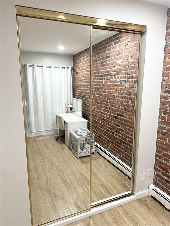 bathroom featuring brick wall, a baseboard heating unit, and hardwood / wood-style flooring