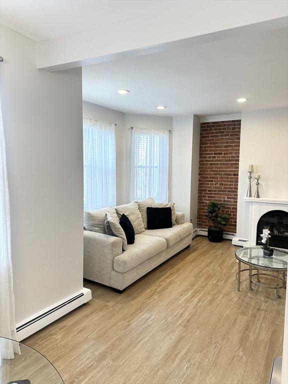 living room with a baseboard heating unit, light hardwood / wood-style floors, and a fireplace